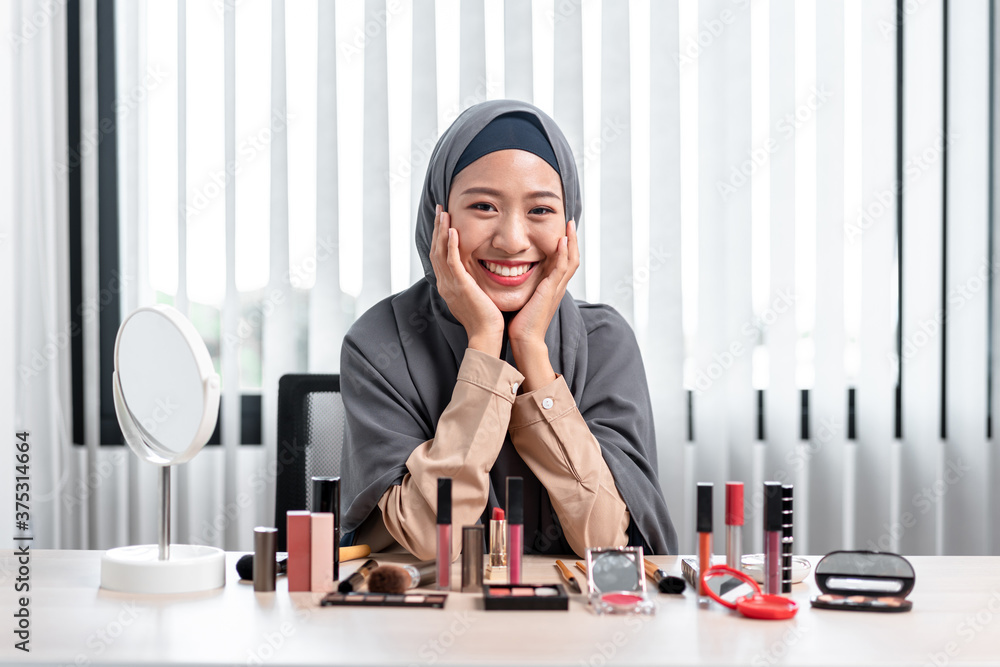 Wall mural portrait of asian muslim woman looking camera and smiling with teaching makeup tutorial online live