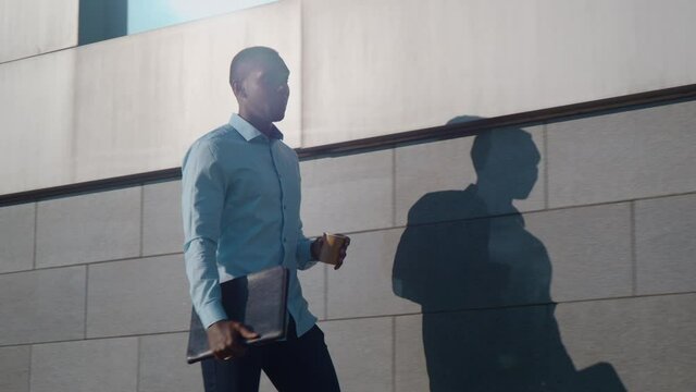 Successful African American business man walks down the street near a business office