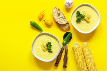 Plates with autumn spicy corn soup. Top view, yellow background. Free space for your text or recipe. Served with corn cobs, chili, bread. 