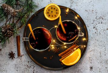 Two glasses of hot mulled wine with oranges and spices with Christmas lights and decorations. Top...