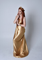 Full length portrait of girl with red hair wearing long grecian toga and golden wreath. Standing...