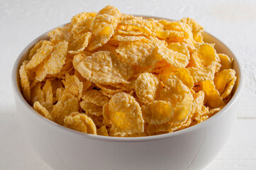 White bowl of cornflakes on a white wooden table.Close-up.