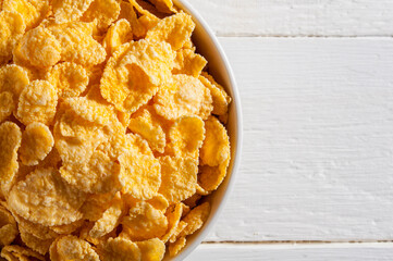 White bowl with cornflakes on a white wooden table. Occupies the left side of the frame. Horizontal frame.