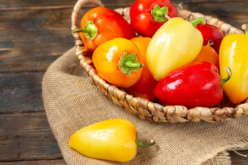 Sweet pepper. Red, yellow and orange peppers in a basket on a brown wooden table. Paprika close up	