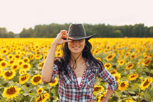 Young woman agronomist wearing cowboy hat, plaid shirt and jeans on sunflower field. Rich harvest concept.