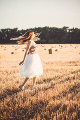 Obraz premium young woman in dress walking in evening in field with hay bales, beautiful romantic girl with long hair outdoors in field
