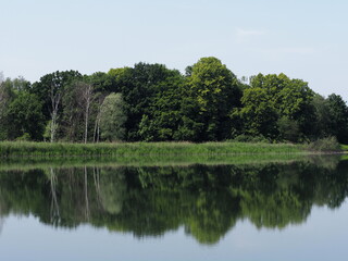 Landscapes reflected in waters of artificial breeding pond in european Goczalkowice town at Silesian district in Poland, clear blue sky in 2020 warm sunny spring day on June.