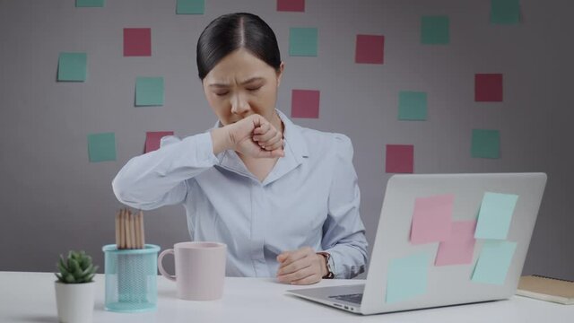 Asian woman working at home office was sick with sore throat and cough in her elbow.