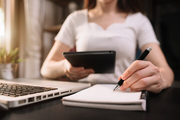Female businessman hand working at a computer and writing on a notepad with a pen in the office.