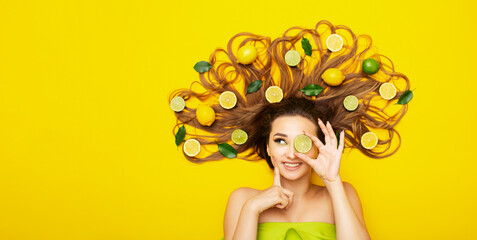 beautiful girl lying on yellow background with citrus fruits in long hair,young woman head with...