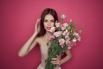 Obraz na płótnie Canvas beautiful woman with a bouquet of flowers on a pink background in a light dress makeup model