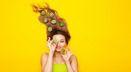 fashion portrait of beautiful girl lying on colored background with kiwi fruit slices on long hair, people and food, young peaceful woman takes care of beauty and body