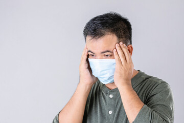 Portrait of Thai patient wearing protective face mask and touching on his head and feel headache. Studio shot on grey