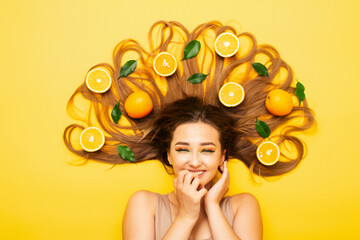happy girl lying on colored background with orange fruits on long hair, young woman sincerely laughs and rejoices