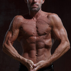 Fototapeta na wymiar A slender, athletic man with a naked muscular torso on a dark background.