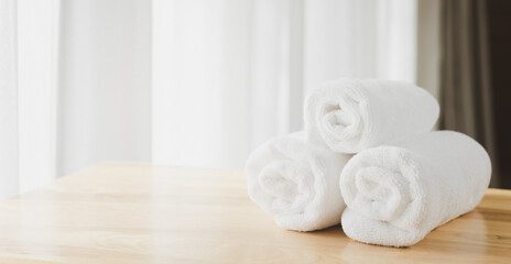 White  soft towels folded on wood table with blurred white bathroom background