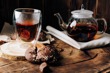 Teapot with black tea and homemade chocolate cookies on a brown natural wooden background