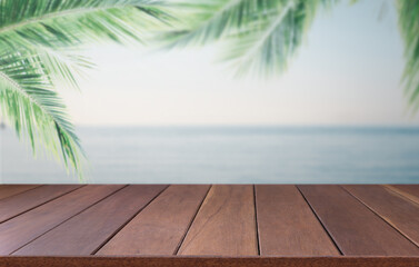 Brown wooden planks with blur beach sky on background and  palm leaves on foreground,summer concepts.