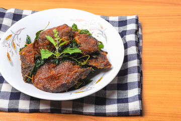 Stir-fried catfish with crispy basil in a white plate on a wooden floor