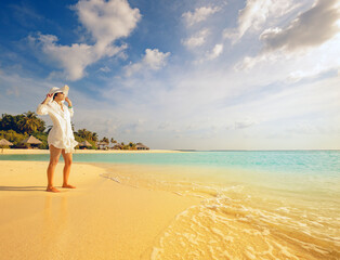 stylish girl watches the sunset on a tropical palm fringed beach of a maldives island with white...