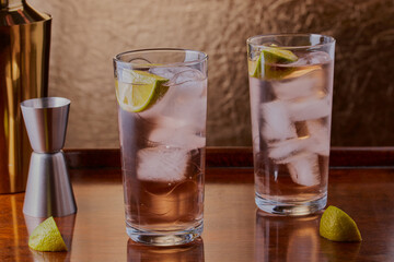 cocktail with ice and lime on wooden drinks tray.