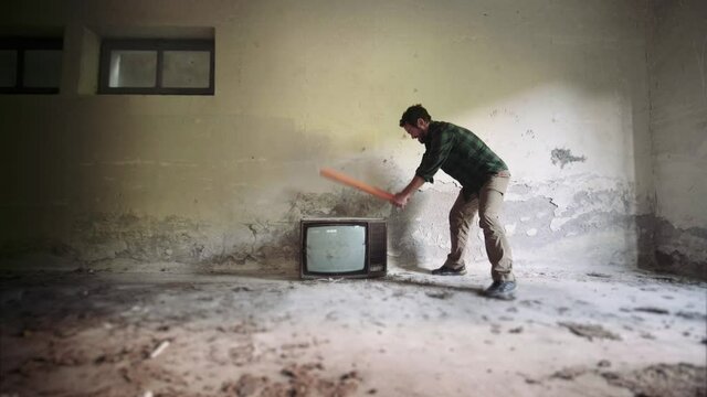 Angry man destroying an old television in an abandoned house. 4k
