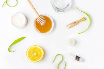 Natural organic ingredients to make home skin care. Cleansing and nourishing cosmetics. Beauty products: cream, honey, sea salt among green leaves on white background. Flat lay, copy space for text