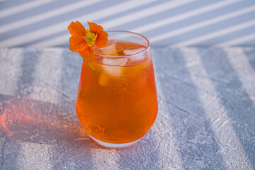 Orange alcoholic cocktail with whiskey, liqueur and orange peel.  Summer refreshing orange drink with ice cubes garnished with edible flowers