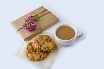 Romantic vintage still life with pretty gift box wrapped with brown craft paper and decorated with pink flower on white background. Dessert (oat cookies) served for tea or coffee brea