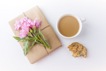 Obraz na płótnie Canvas Romantic vintage still life with pretty gift box wrapped with brown craft paper and decorated with pink flower on white background. Dessert (oat cookies) served for tea or coffee break.