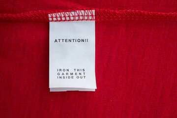 Fototapeta na wymiar White laundry care washing instructions clothes label on red cotton shirt
