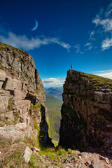 Fototapeta na wymiar Tourist standing on edge taking in views over Torridon mountains with moon in view. located in the highlands of Scotland.