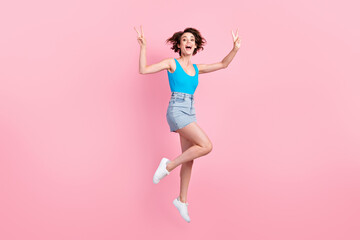 Fototapeta na wymiar Full body size photo of pretty charming sporty young lady smiling open mouth jump raise hands showing v-sign wear denim mini skirt blue singlet sneakers isolated pink color background