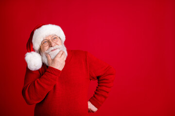 Fototapeta na wymiar Photo of dreamy thoughtful old man in santa claus headwear look copyspace touch hand chin think jolly holly gifts wear style jumper isolated over bright shine color background
