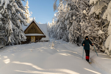 Man walking in sunny snowy mountains with wooden house on background