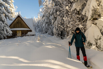 Man walking in sunny snowy mountains with wooden house on background