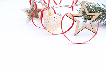 Christmas composition of fir branches, wooden stars, garlands of white luminous balls and red ribbon on a white background.