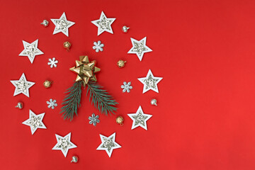 Flat composition of Christmas decorations in white and gold and fir branches on a red background.