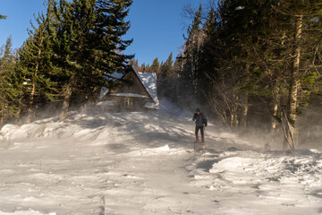 Man walking in sunny snowy mountains with wooden house on background