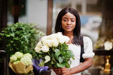 Beautiful african american girl holding bouquet of white roses flowers on dating in the city. Black businesswoman with bunch of flowers.