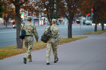 Belarus soldiers in camouflage dress walking through the street in the center of Minsk with bags behind back, rear view. Group of soldiers. Military men in uniform.