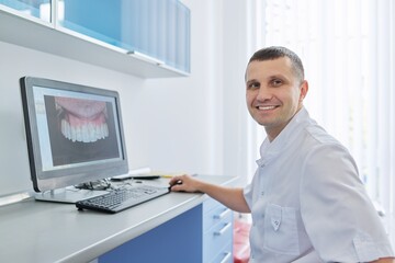 Portrait of male dentist, sitting working with computer in dental clinic