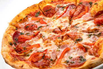 pizza with ham, sausage and tomatoes on a white plate