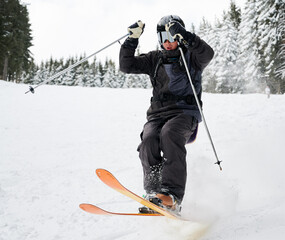 Man skier in black ski suit and goggles skiing downhill trough deep powder snow. Young man freerider in helmet using ski poles and gliding on snow at ski resort. Concept of skiing and active leisure.