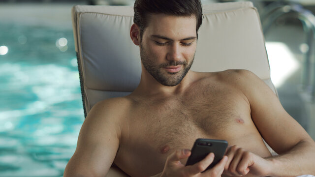 Closeup man looking phone by pool. Male relaxing with phone at wellness center - Powered by Adobe