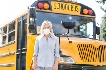Portrait of beautiful female masked teacher near school bus