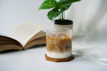 Iced latte coffee. A cup of latte coffee with milk and espresso shot with book and small tree decoration on white background.