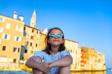 Fototapeta na wymiar Funny little girl in sunglasses on sunny summer day. Rovinj town in background. Summer vacation at sea.