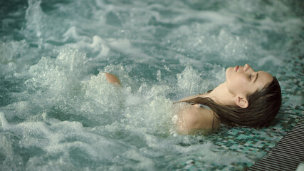 Young woman relaxing in pool at luxury spa. Beautiful girl bathing at jacuzzi - obrazy, fototapety, plakaty