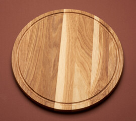 new empty round wooden cutting board on brown background